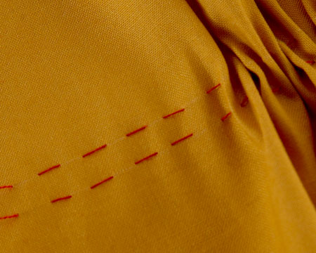 Two lines of running stitch being pulled to gather from one end.